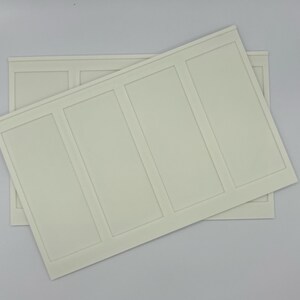May include: Two off-white rectangular wall panels with a raised rectangular design. One panel is partially covering the other. The panels have a smooth surface and are set against a white background.