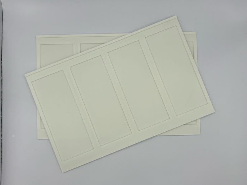 May include: Two off-white rectangular wall panels with a raised rectangular design. One panel is partially covering the other. The panels have a smooth surface and are set against a white background.