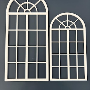 Puede incluir: Dos marcos de ventana blancos con la parte superior arqueada. El marco más grande mide aproximadamente 46 cm de alto, mientras que el más pequeño mide unos 30 cm. Ambos presentan un patrón de rejilla de paneles rectangulares y una parte superior semicircular con un diseño de abanico. Las ventanas están sobre un fondo azul oscuro.
