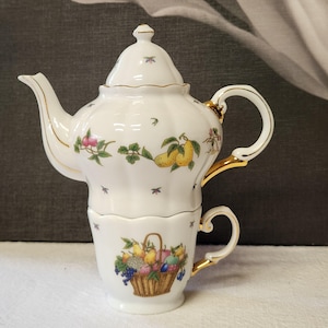 May include: White porcelain tea-for-one set with a teapot and teacup. The teapot features a lid and is decorated with fruit and floral designs, with gold trim. The teacup has a handle and a basket of fruit design.