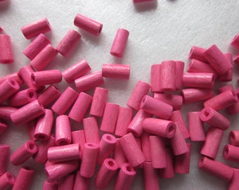 Puede incluir: Un gran grupo de cuentas de madera de color rosa, todas de forma cilíndrica, están esparcidas sobre una superficie blanca. Las cuentas son lisas y tienen un ligero brillo.