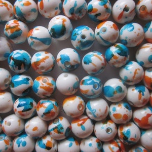 May include: A collection of white round beads with blue and orange paint splatters. The beads are arranged in a circular pattern.