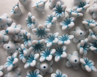 Puede incluir: Una colección de cuentas blancas con forma de flor con acentos azul turquesa. Las cuentas tienen un agujero en el centro para enhebrar.