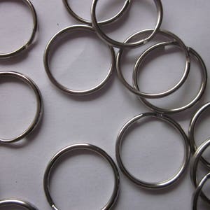 Könnte beinhalten: Nahaufnahme eines Stapels silberner Schlüsselringe. Die Schlüsselringe sind alle in verschiedenen Größen und Formen, aber alle aus dem gleichen Metall.