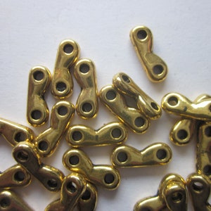 May include: A pile of gold-colored metal connector charms with two holes each. The charms are shaped like a sideways figure eight.