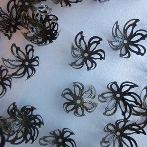 Pu&ograve; includere: Una collezione di decorazioni in metallo nero a forma di fiore con disegni intricati. Questi pezzi decorativi sono perfetti per aggiungere un tocco di eleganza ad artigianato e gioielli.