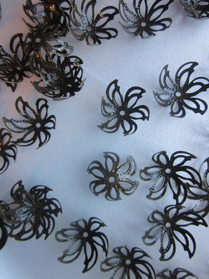Pu&ograve; includere: Una collezione di decorazioni in metallo nero a forma di fiore con disegni intricati. Questi pezzi decorativi sono perfetti per aggiungere un tocco di eleganza ad artigianato e gioielli.