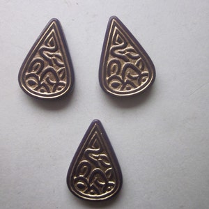 May include: Three purple teardrop-shaped pendants with a gold Celtic knot design.