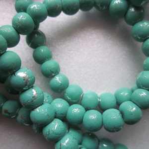 May include: A strand of turquoise blue beads with silver accents. The beads are round and have a slightly textured surface.