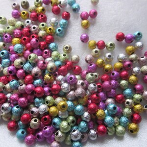 May include: A large assortment of colorful, metallic beads. The beads are round and have a textured surface. They are a mix of silver, gold, pink, blue, green, and red.