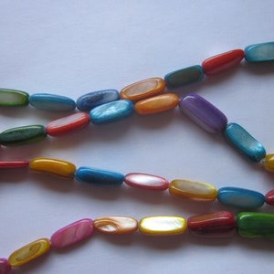 May include: A strand of colorful oval-shaped beads made from mother of pearl. The beads are in shades of blue, green, red, orange, yellow, and purple.