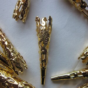 May include: A group of gold metal decorative tips with intricate designs. The tips are cone-shaped and have a filigree pattern.