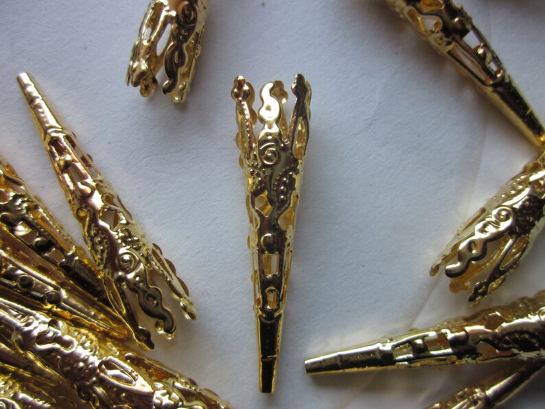 May include: A group of gold metal decorative tips with intricate designs. The tips are cone-shaped and have a filigree pattern.