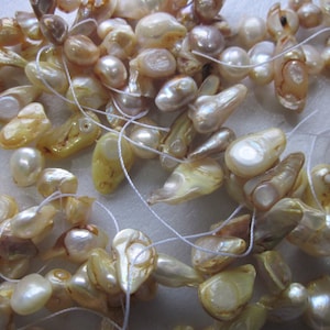 May include: A strand of off-white baroque pearls with an iridescent sheen. The pearls are strung on white thread and are various shapes and sizes.