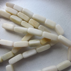 Könnte beinhalten: Eine Schnur aus rechteckigen Perlen in gebrochenem Weiß aus Naturstein. Die Perlen sind glatt und leicht durchscheinend.