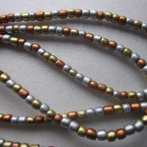 May include: A close-up of a beaded necklace with alternating silver, gold, and copper colored beads.