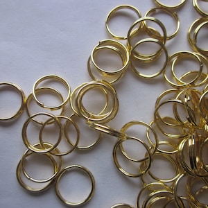 Könnte beinhalten: Ein großer Haufen goldfarbener Schlüsselringe aus Metall. Die Schlüsselringe sind alle gleich groß und gleich geformt und in einem zufälligen Muster angeordnet.