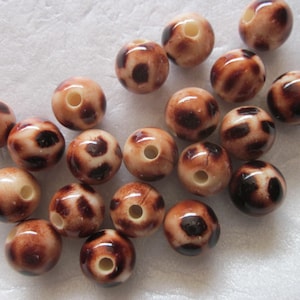 Puede incluir: Un conjunto de cuentas redondas con un acabado brillante. Las cuentas son de color beige con manchas marrones oscuras, que se asemejan a un estampado de leopardo. Cada cuenta tiene un agujero en el centro. Estas cuentas son adecuadas para la fabricación de joyas.