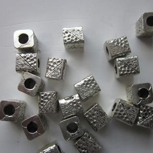 Puede incluir: Cuentas cúbicas plateadas dispersas con superficies texturizadas y agujeros pasantes. Algunos cubos tienen una textura martillada, mientras que otros presentan un diseño de línea diagonal. Adecuado para la fabricación de joyas y manualidades.
