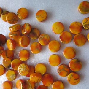 May include: A collection of round, orange and yellow beads with gold accents. The beads have a marbled effect and are perfect for jewelry making.