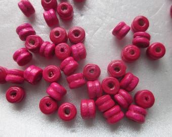 Puede incluir: Una colección de cuentas de madera de color rosa brillante, cada una con un agujero en el centro. Las cuentas son redondas y tienen un acabado liso y pulido.