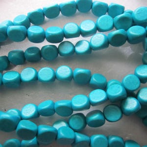 May include: Close-up of several strands of turquoise-colored, cube-shaped beads. The beads are strung together, creating a necklace or bracelet. The beads have a smooth, rounded appearance and are a vibrant shade of blue-green.