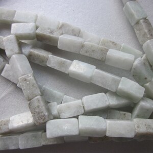 Puede incluir: Una hebra de cuentas de jade verde claro y blanco, cada cuenta es un prisma rectangular con bordes ligeramente redondeados.