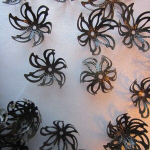Pu&ograve; includere: Una collezione di decorazioni decorative in metallo nero a forma di fiore con una finitura testurizzata.
