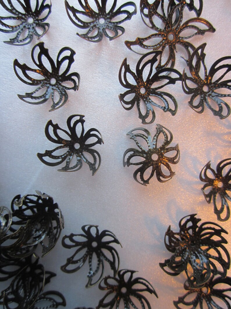 Pu&ograve; includere: Una collezione di decorazioni decorative in metallo nero a forma di fiore con una finitura testurizzata.