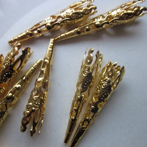 May include: A group of gold-colored metal bead caps with intricate designs. The caps are cone-shaped and have a decorative, openwork pattern.