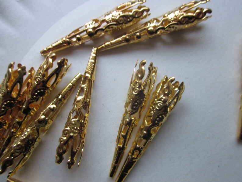 May include: A group of gold-colored metal bead caps with intricate designs. The caps are cone-shaped and have a decorative, openwork pattern.