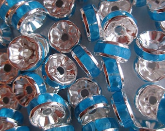May include: A close-up of a pile of silver and turquoise blue metal bead caps. The bead caps have a decorative design and are perfect for jewelry making.
