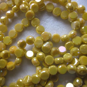 May include: A strand of yellow iridescent glass beads. The beads are faceted and have a round shape.
