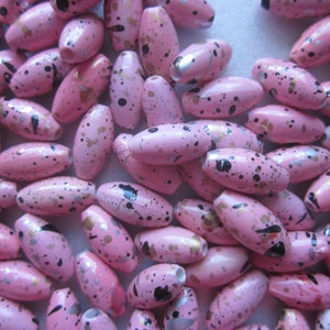 May include: Pink oval-shaped wooden beads with black, gold, and silver paint splatters.