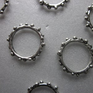 May include: Close-up of several silver-colored rings. Each ring has a textured, beaded design around the band. The rings are scattered on a light gray surface, with some rings overlapping.