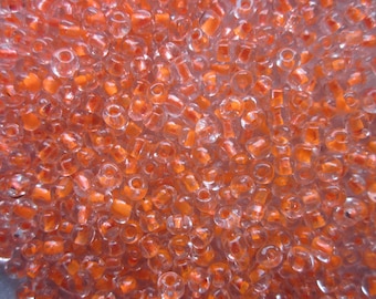 May include: A close-up of a large quantity of small, clear glass beads with an orange iridescent finish.