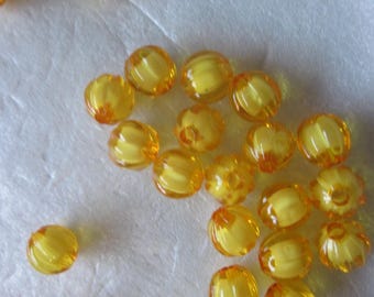 Puede incluir: Un conjunto de cuentas translúcidas de color amarillo-naranja dispersas sobre una superficie blanca. Las cuentas tienen una textura acanalada y una forma irregular. El color es consistente, con un tono cálido y soleado. Adecuado para bisutería.