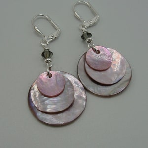 May include: A pair of silver earrings with three layered iridescent pink and white shell circles hanging from a silver hook. Each earring has a small black crystal bead.