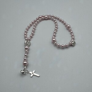 May include: A pink beaded rosary with a silver cross pendant and a magnetic clasp. The rosary features a silver centerpiece with a religious figure. The beads are a soft pink color.