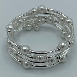 May include: A silver-toned, multi-strand wrap bracelet featuring faux pearls. The bracelet has multiple coiled strands with evenly spaced, round, white pearls and decorative silver accents. The bracelet is designed to wrap around the wrist.