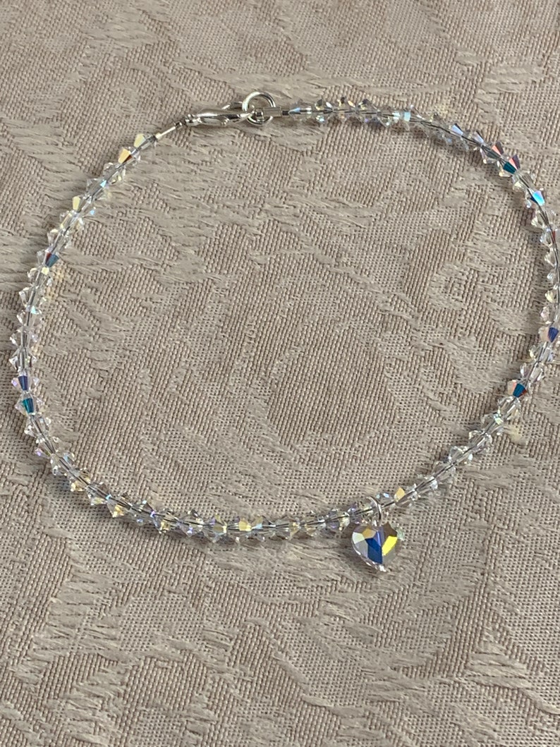 Pu&ograve; includere: Una delicata cavigliera di cristallo trasparente con un piccolo ciondolo a forma di cuore. La cavigliera &egrave; composta da piccoli cristalli sfaccettati infilati con una catena e chiusura color argento. Il ciondolo a forma di cuore riflette pi&ugrave; colori.