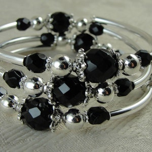 May include: A silver bangle bracelet with black faceted beads and silver spacer beads. The bracelet is made of multiple strands of silver wire.