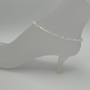 May include: A delicate crystal anklet with a clear, iridescent finish. The anklet is made of small, faceted crystals that are strung together on a thin silver chain.