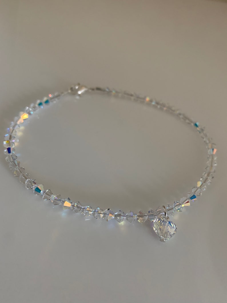 Pu&ograve; includere: Una delicata cavigliera di cristallo trasparente con un ciondolo a forma di cuore. La cavigliera &egrave; composta da piccoli cristalli sfaccettati che riflettono la luce. Il ciondolo a forma di cuore &egrave; anch'esso in cristallo trasparente.