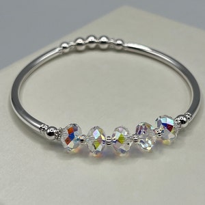 May include: A silver bangle bracelet with a row of clear crystal beads. The bracelet is made of a thin, round wire and has a simple, elegant design.