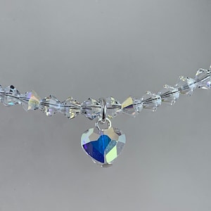 Pu&ograve; includere: Una collana di cristallo trasparente con un ciondolo a forma di cuore. Il ciondolo e le perle della collana riflettono un arcobaleno di colori. La collana &egrave; infilata su un filo trasparente.