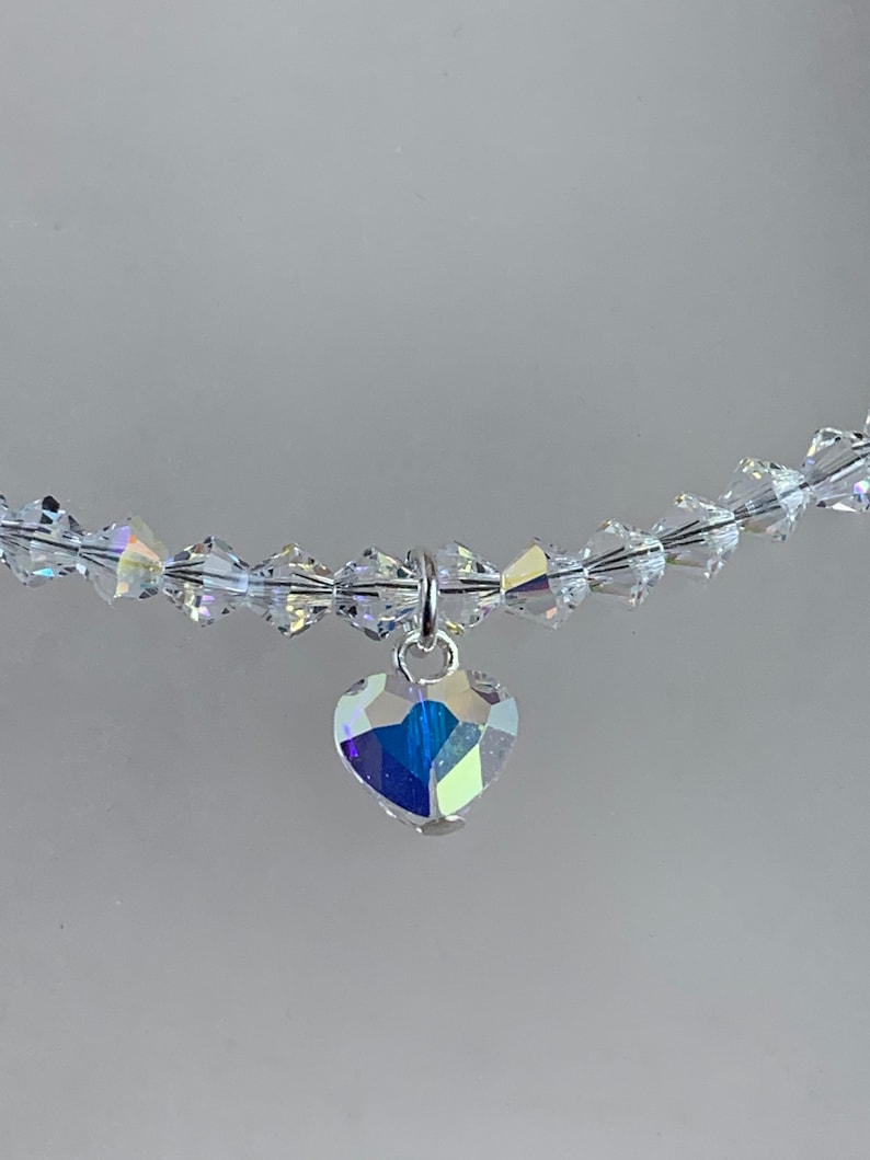 Pu&ograve; includere: Una collana di cristallo trasparente con un ciondolo a forma di cuore. Il ciondolo e le perle della collana riflettono un arcobaleno di colori. La collana &egrave; infilata su un filo trasparente.