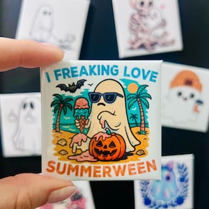 May include: Square magnet with a cartoon ghost wearing sunglasses, holding an ice cream cone, and a jack-o'-lantern. The text reads "I FREAKING LOVE SUMMERWEEN". Other magnets with ghost and skeleton designs are in the background.