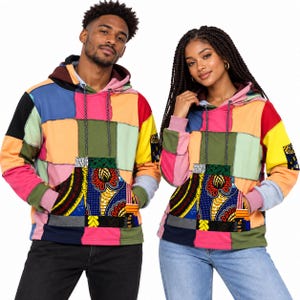 Könnte beinhalten: Ein langärmeliger Kapuzenpullover mit einem Patchwork-Design aus verschiedenen Unifarben wie Pink, Orange, Gelb, Grün und Blau. Die Vorderseite verfügt über eine große Kängurutasche mit einem lebendigen, bunten Blumenmuster.