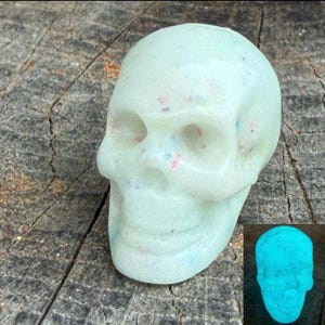 Könnte beinhalten: Eine blass minzgrüne Totenkopffigur mit kleinen, mehrfarbigen Sprenkeln auf der gesamten Oberfläche. Der Totenkopf hat hohle Augenhöhlen, eine Nasenhöhle und einen definierten Kiefer. Ein Inset zeigt denselben Totenkopf in leuchtendem Cyan.